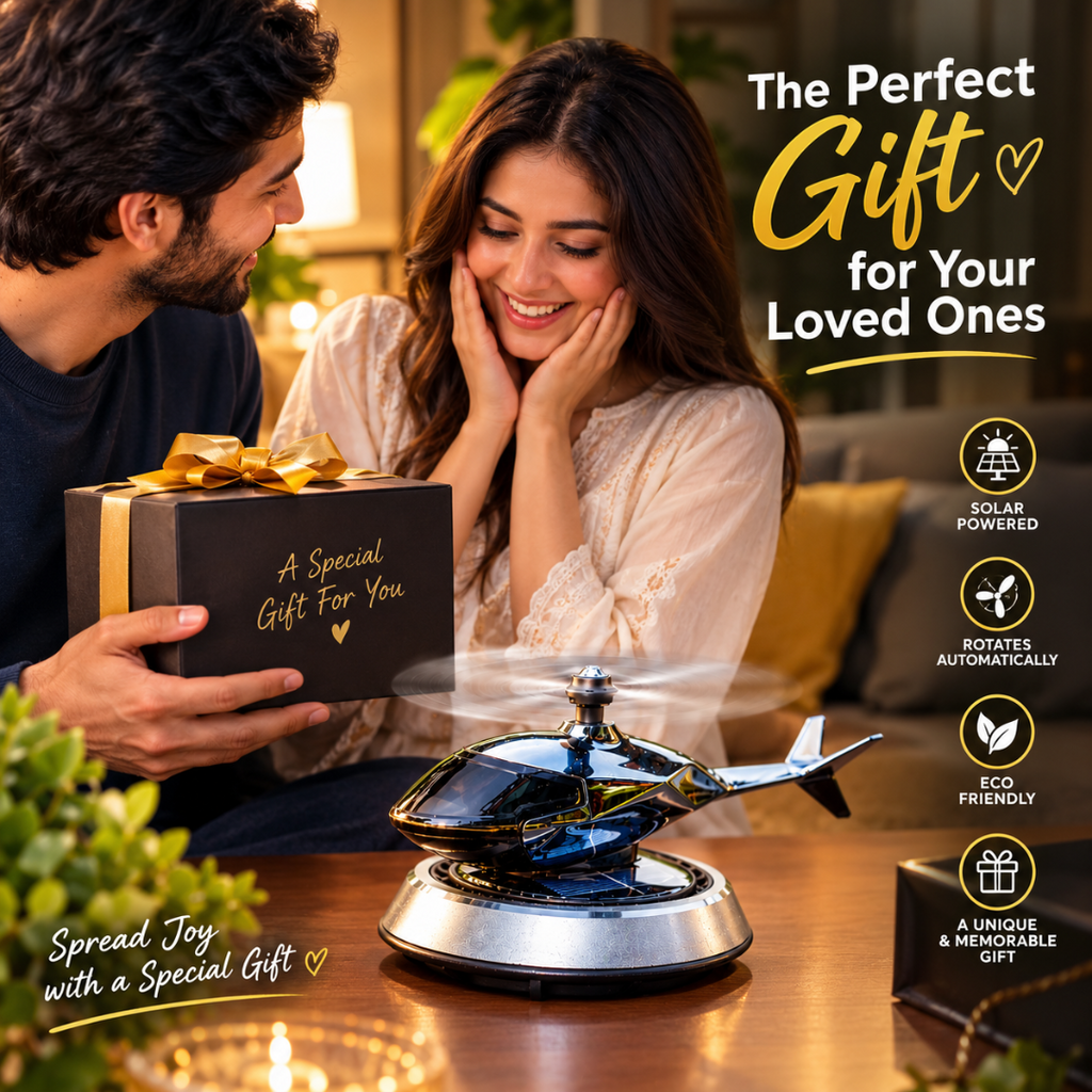 A man presents a black gift box with gold lettering to a woman in a warmly lit living room. In the foreground, a blue and black helicopter-shaped solar-powered gift toy spins on a tabletop.