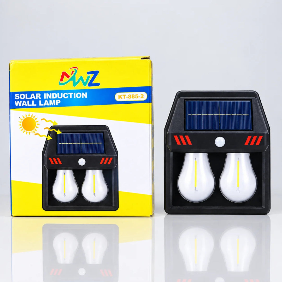 A solar induction wall lamp shown next to its yellow and white retail box. The lamp has a black body, a blue solar panel on top, and two white bulb-shaped light compartments with yellow LED strips.