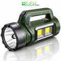 A tactical LED flashlight in olive green and black, featuring a built-in handle, a large front lens, and two bright yellow LED light panels on the side. The ILEX biz logo is visible at the top of the image.