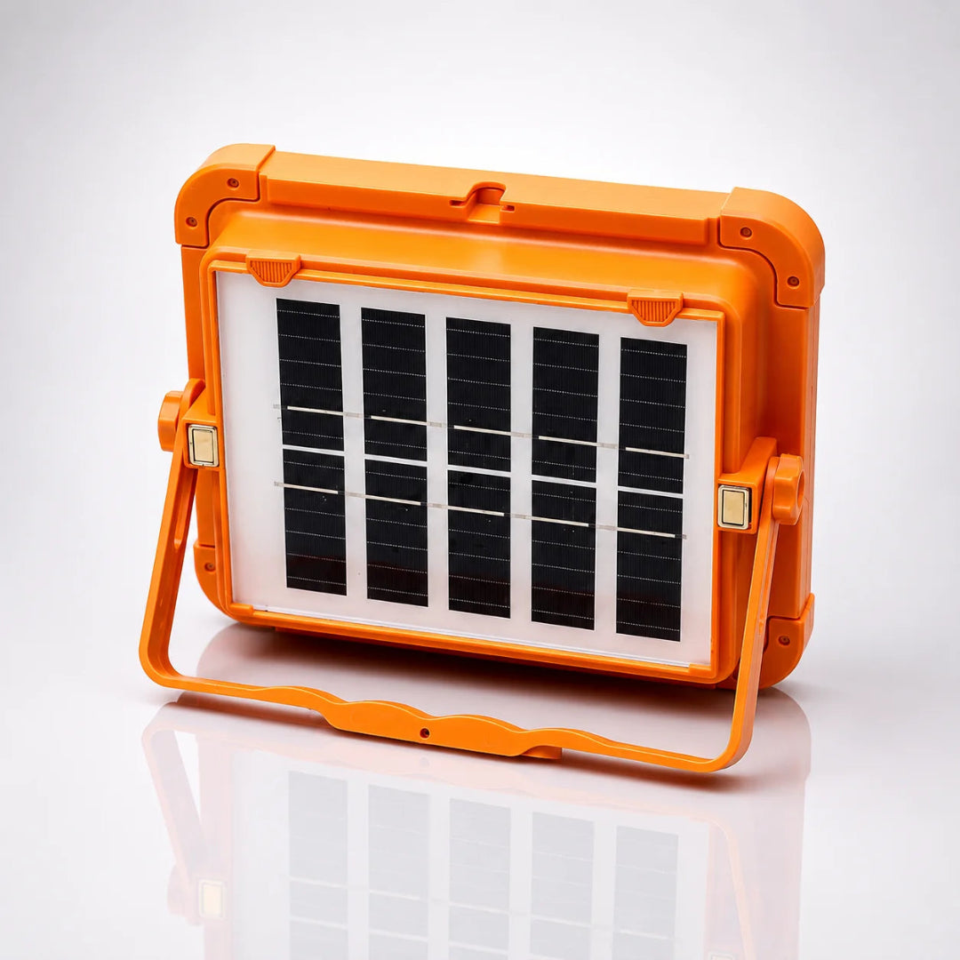 An orange portable solar light with a built-in handle and a front panel of five black solar cells, shown on a reflective white surface.