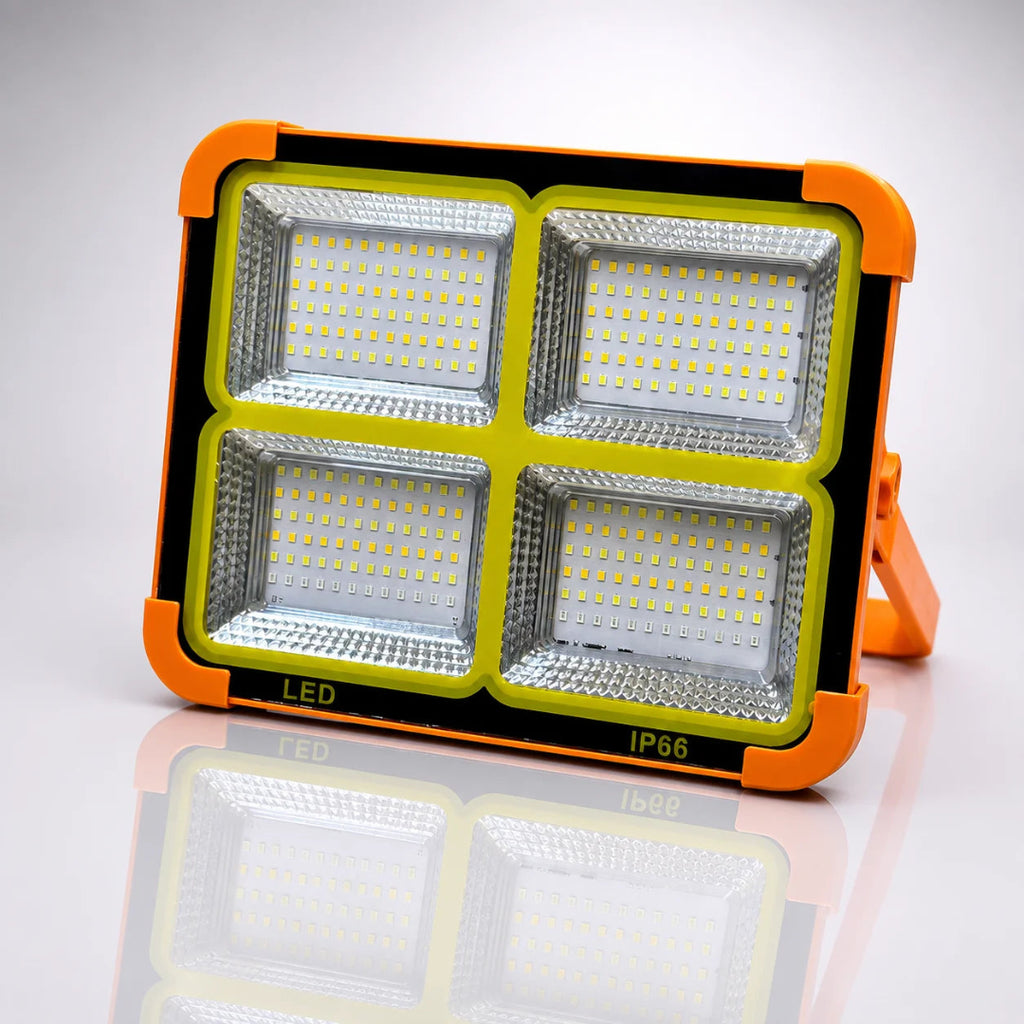 A rugged outdoor LED floodlight with a bright orange protective casing, four large square LED panels, and a small mounting bracket, shown on a reflective white studio background.