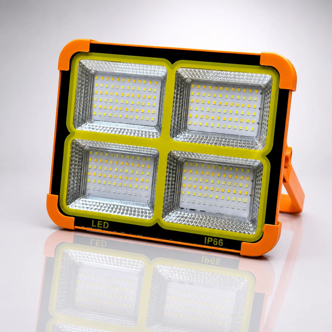 A rugged outdoor LED floodlight with a bright orange protective casing, four large square LED panels, and a small mounting bracket, shown on a reflective white studio background.