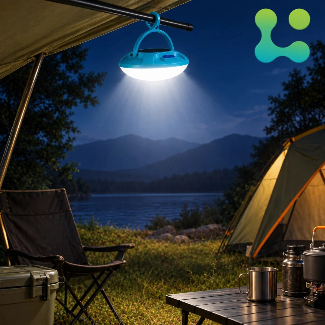 A blue camping lantern with an integrated LED light hanging from a tent pole at night by a lake, with a camping chair, table, cooler, and tent in the background. A green and blue logo is in the top right corner.