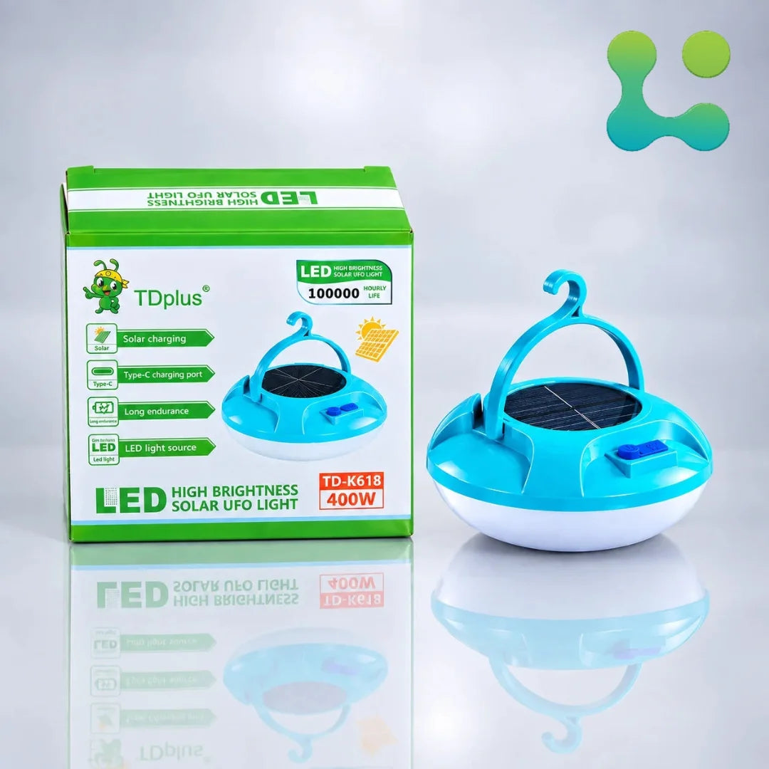 A turquoise and white solar-powered LED UFO light shown next to its green and white retail box on a reflective white surface, with a teal logo in the top right corner.