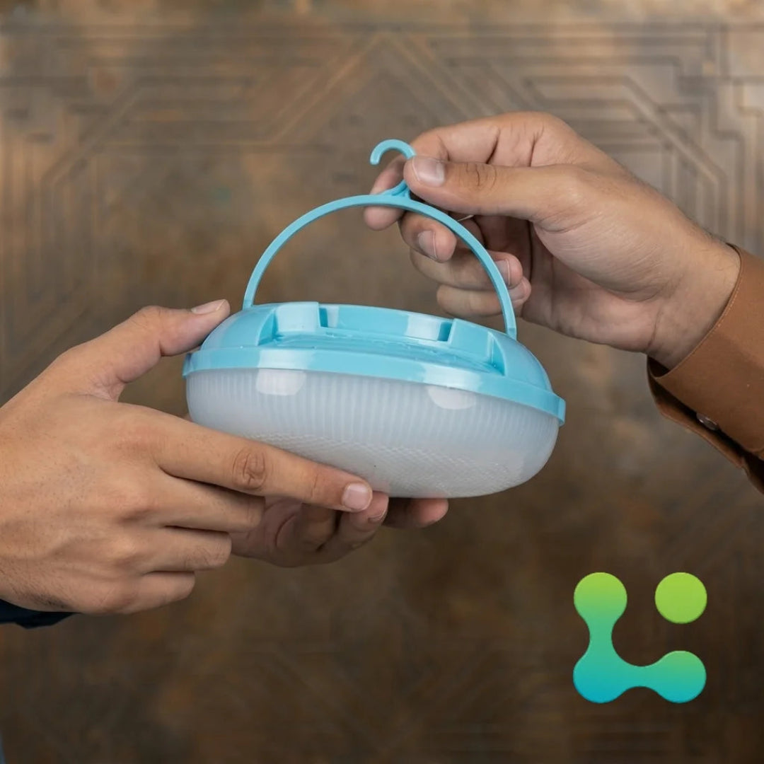 A person's hands holding a round, ribbed translucent white container with a light blue lid, carrying handle, and hook at the top, set against a textured brown background.