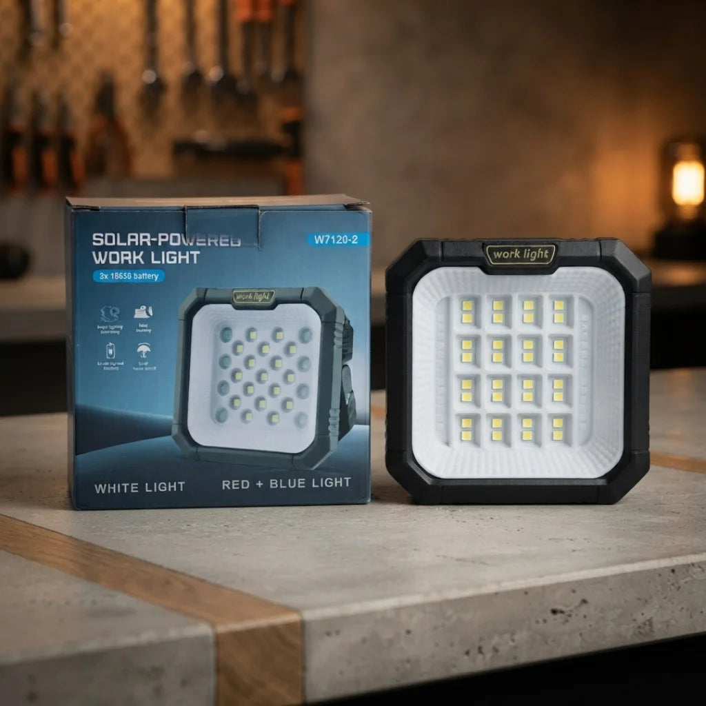 A solar-powered work light shown next to its retail box on a stone countertop in a kitchen setting. The work light has a black body, a white front panel with multiple LED chips, and a small brand label reading 'work.